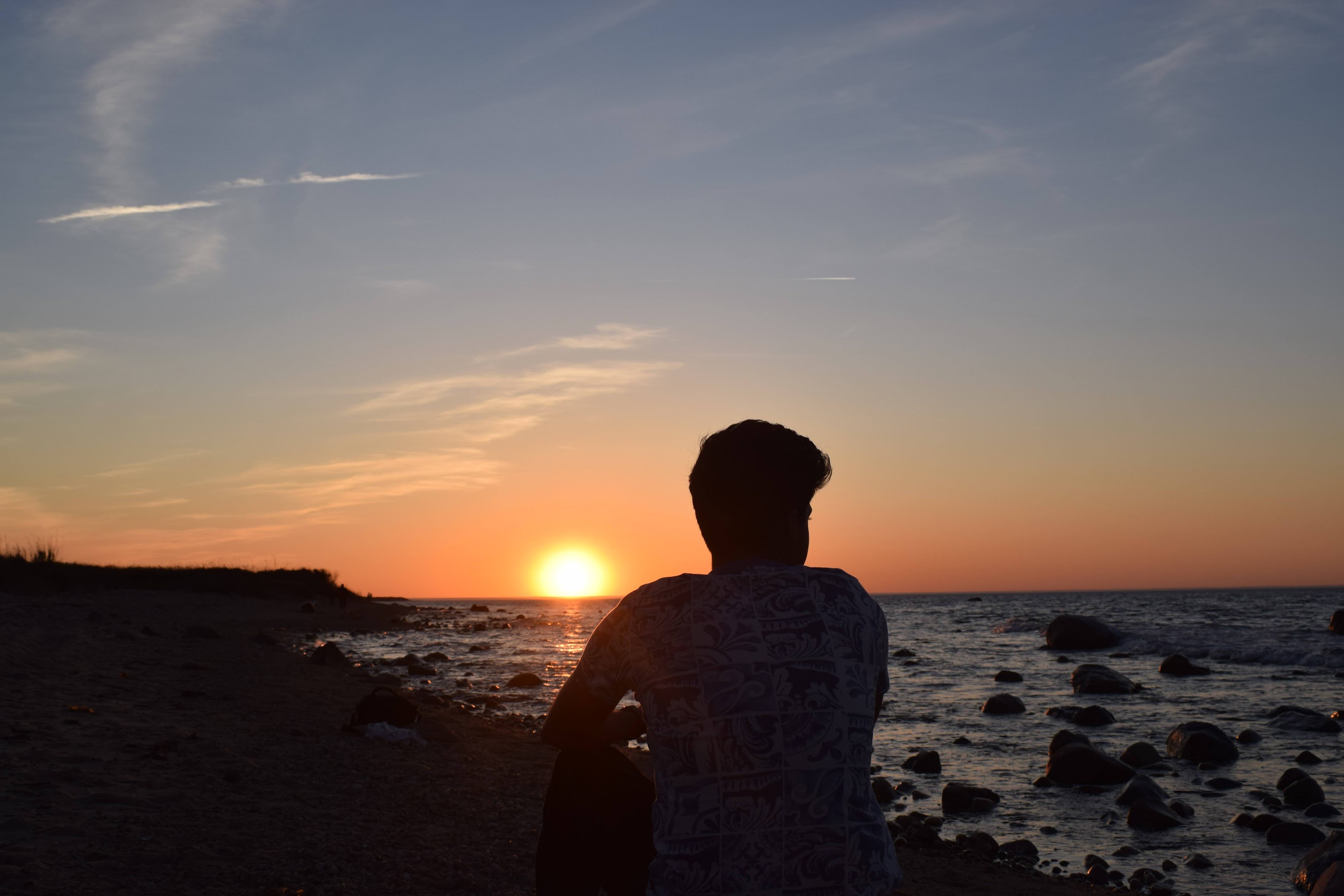 A person looking toward the setting sun from a rocky beach