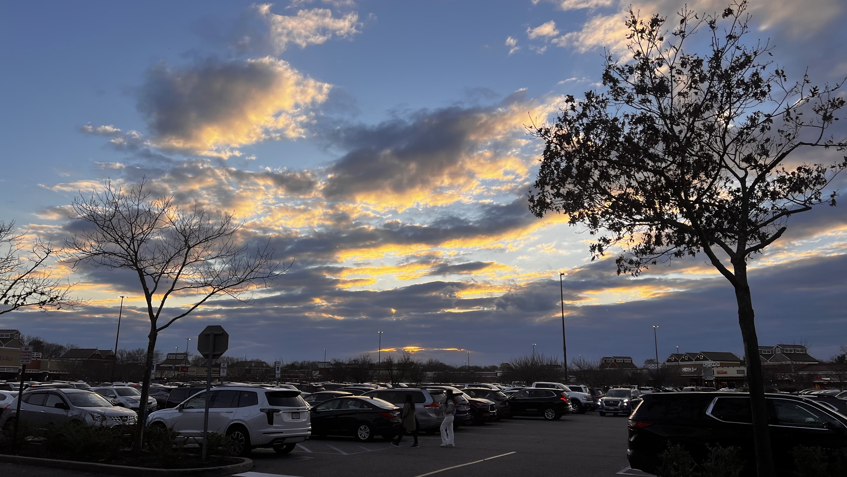 Golden sunset clouds above trees and a busy parking lot